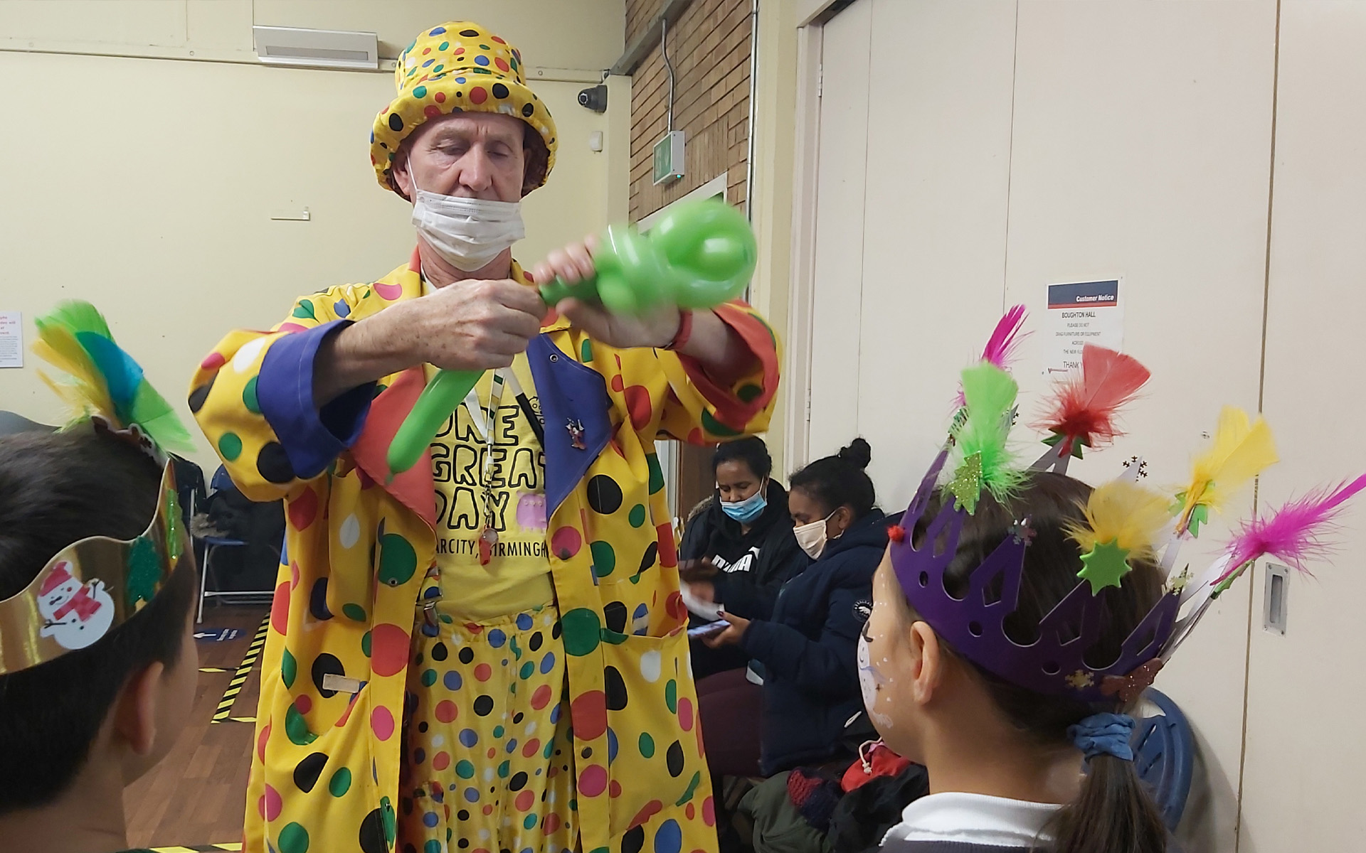A clown creating balloon animals for children at a Christmas party.