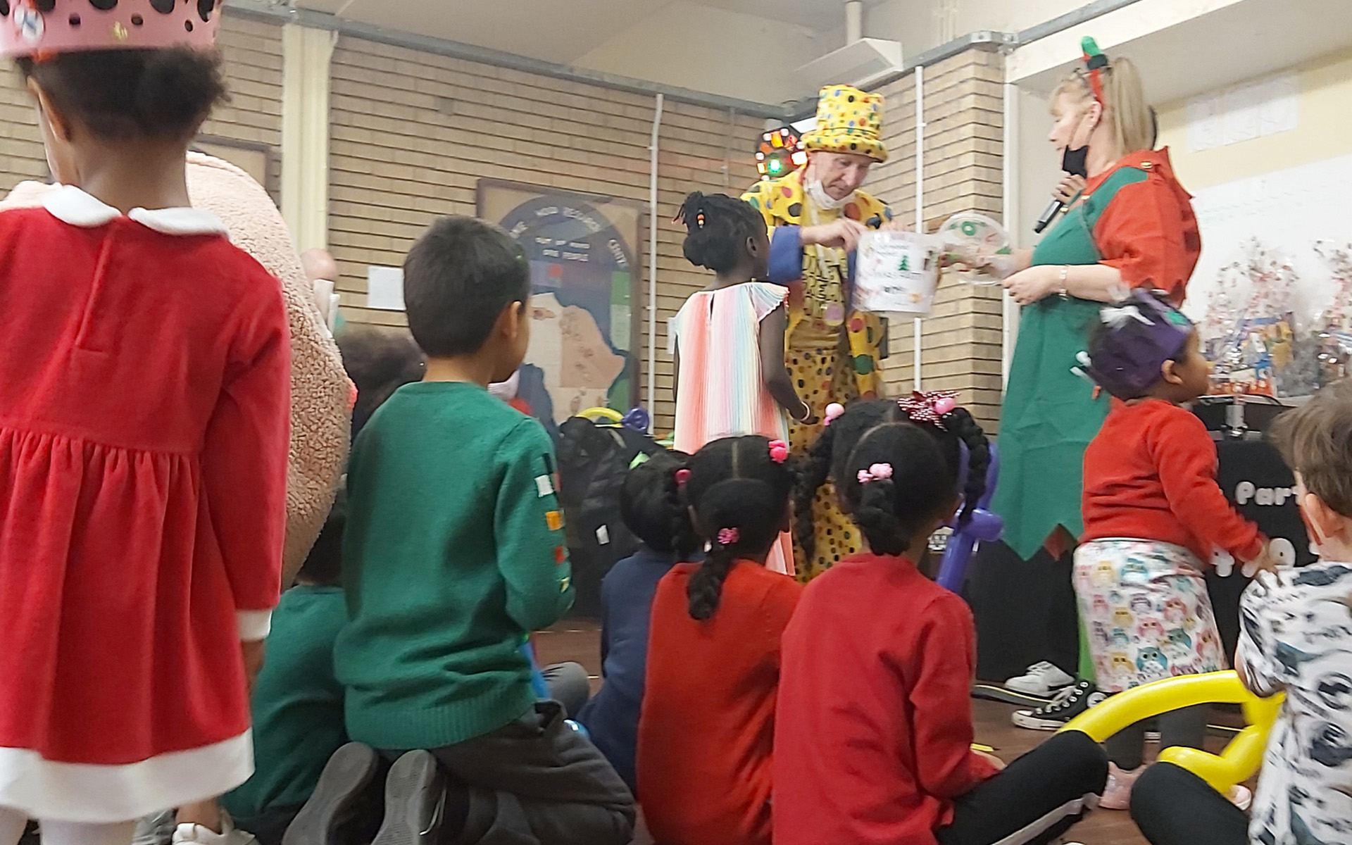 Children watching a clown perform a prize draw at a Christmas party.