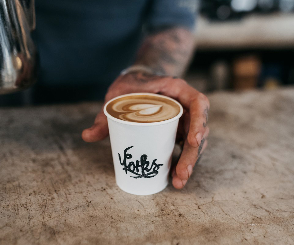 A cup of coffee, with the Yorks logo on, with a decorative swirl pattern.