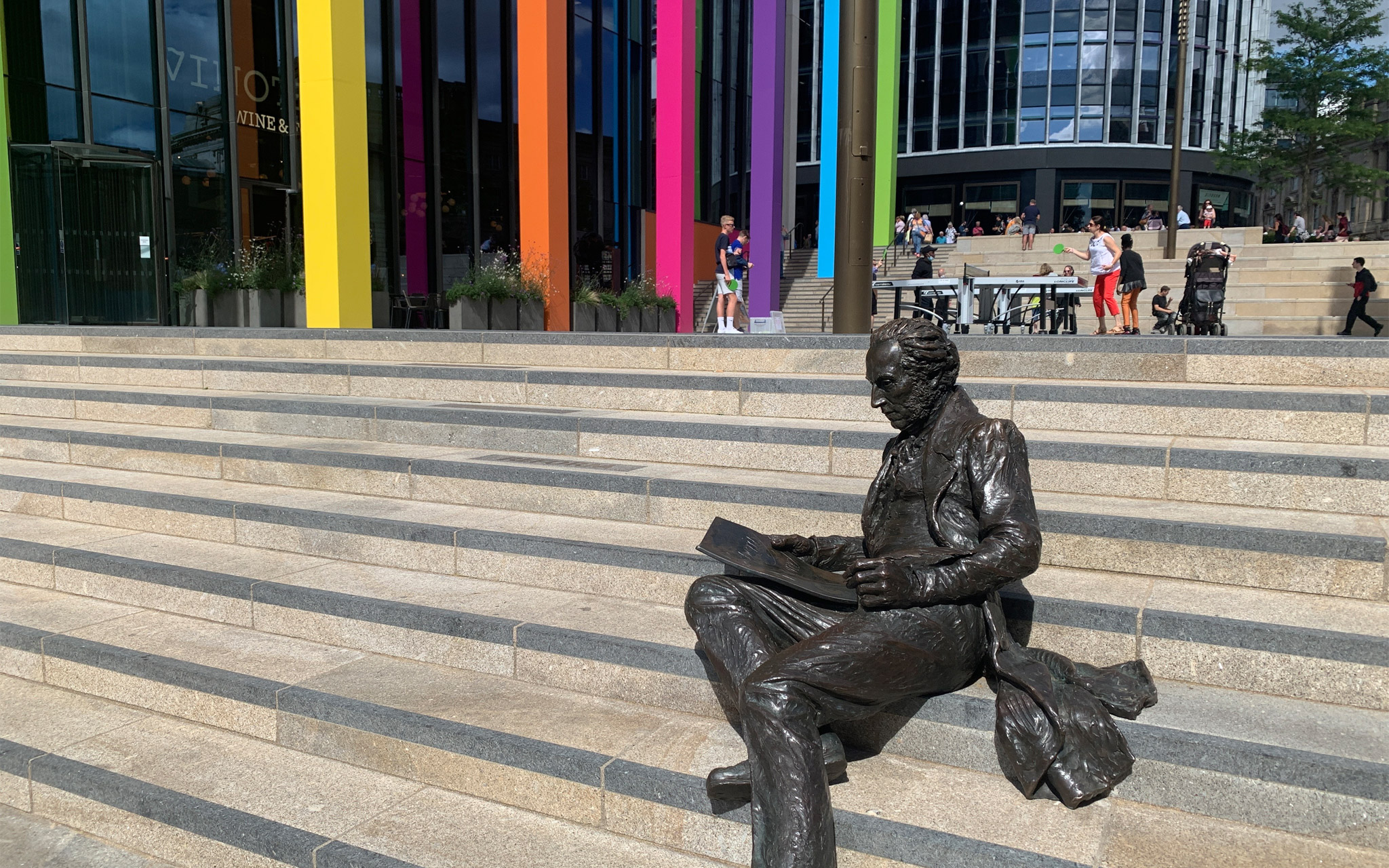 Thomas Attwood statue in Chamberlain Square, Paradise Birmingham. The columns of Two Chamberlain Square are painted in the Commonwealth Games colours behind him.