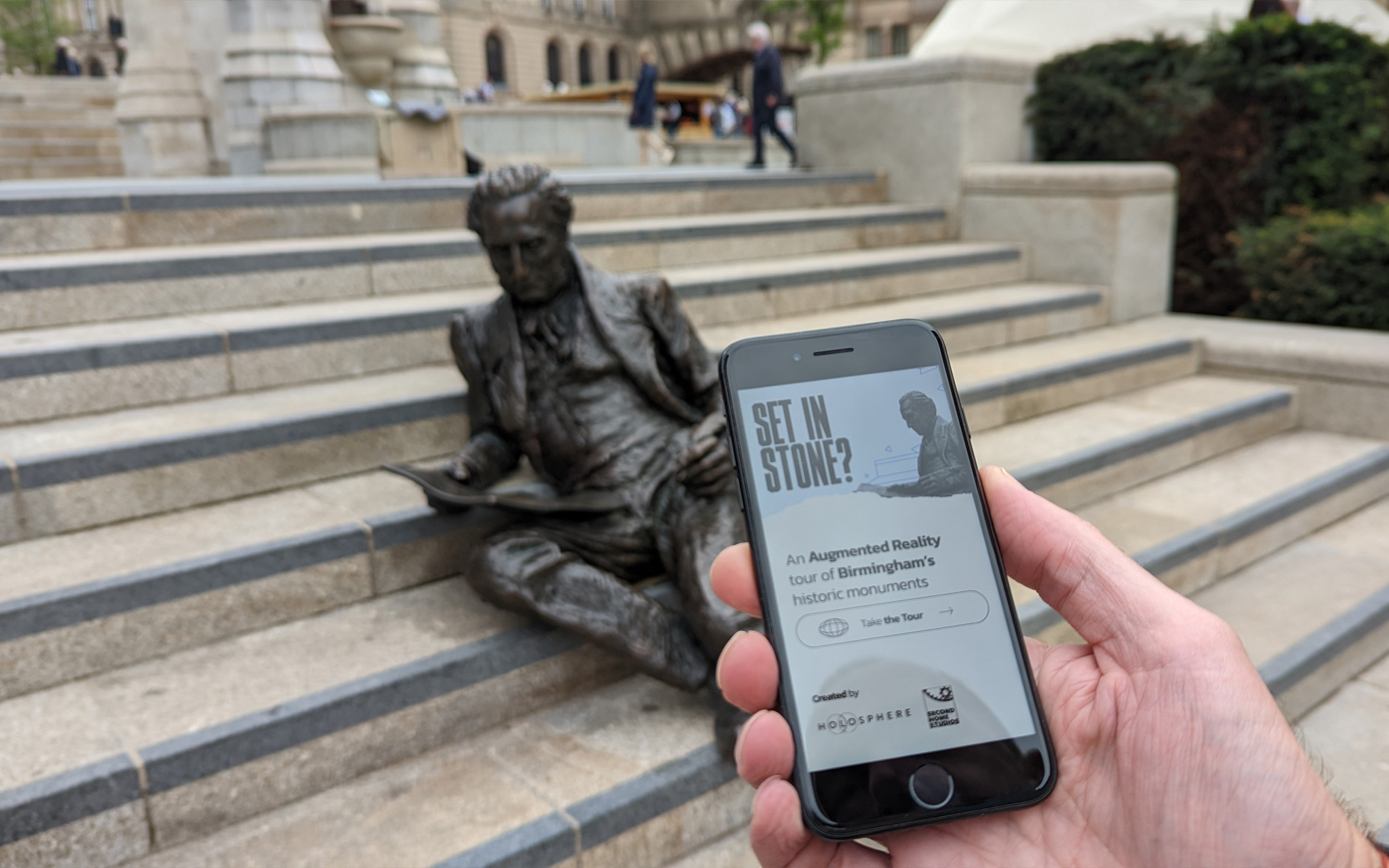 Someone using a mobile phone with augmented reality to find out more about the statues in Chamberlain Square, Paradise.